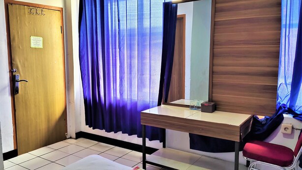 A room with a wooden door, a desk with a mirror, a red chair, and a striped rug. - De' Premium Hotel Musi Raya (Palembang)