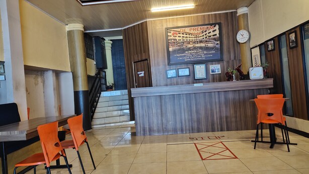 Zona de recepción de un hotel con un mostrador de madera, sillas anaranjadas, una escalera y un reloj en la pared.