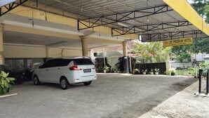 Un SUV blanco estacionado bajo un toldo amarillo en la entrada de un hotel.