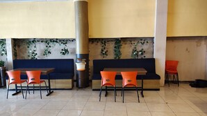 Un café con un sofá azul, sillas naranjas y plantas colgantes.
