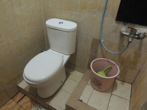 A toilet with a bidet attachment and a pink bucket with a green handle.