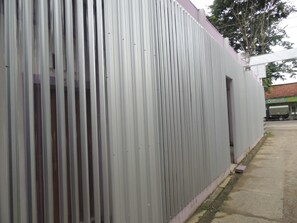 A corrugated metal wall with a small door and a concrete pathway.
