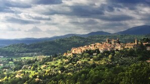 Una cittadina storica con architettura medievale, immersa in dolci colline verdi e un cielo nuvoloso.
