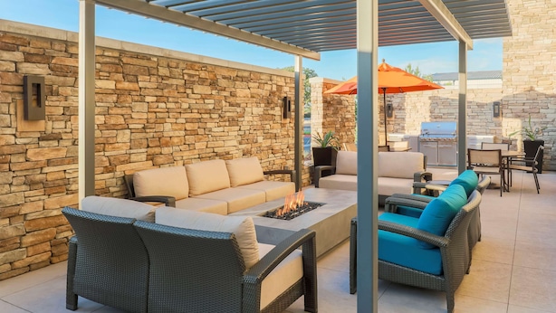 An outdoor patio with stone walls, wicker furniture, and a grill area. - Hyatt House Davis (Davis)