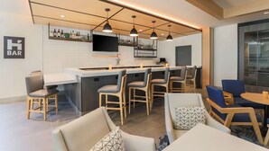 A modern bar area with a long counter, multiple bar stools, and a television mounted on the wall. - Hyatt House Davis (Davis)