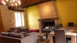 Una sala de estar acogedora con un sofá, una mesa de comedor con sillas, una chimenea y una araña.