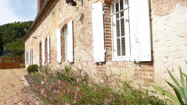 Un edificio rústico de piedra con contraventanas blancas y una chimenea de ladrillo.
