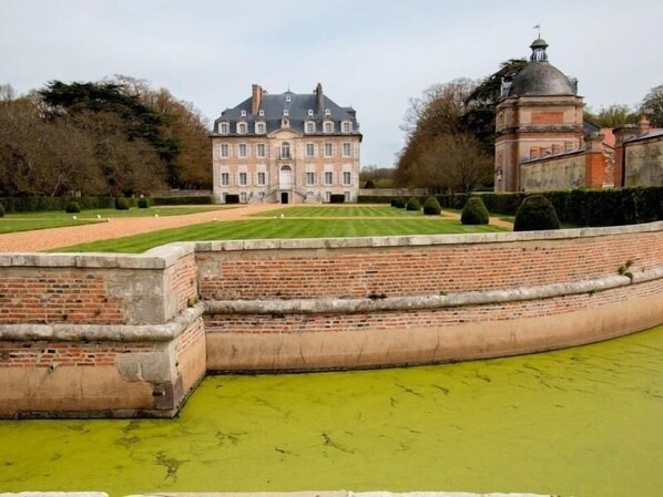 A large, historic building with a symmetrical facade, a central entrance, and a formal garden with trimmed hedges. - Charming 12-Person Cottage with Garden, BBQ & Bikes near Chartres (Les-Villages-Vovéens)