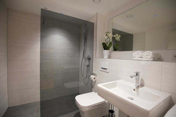 Un baño moderno con ducha acristalada, lavamanos blanco y retrete.