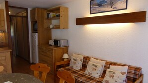 Ein gemütliches Zimmer mit einem karierten Sofa, Holzstühlen, einem kleinen Tisch und einer Mikrowelle auf einem Holzschrank.