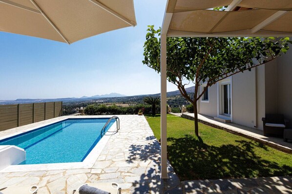 A swimming pool with a stone deck, a tree, and a view of distant mountains.