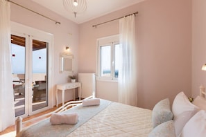 A bedroom with a bed, a bedside table, a mirror, a window, and a view of the outside.