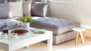 Ein modernes Wohnzimmer mit einer Couch, einem Couchtisch, einer Blumenvase, einer Korb mit Erdbeeren und einer Zeitschrift.