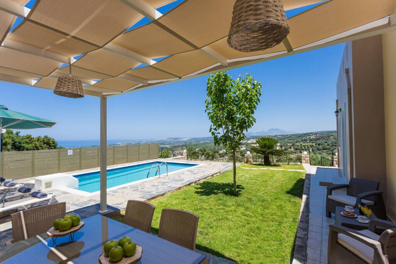 A poolside area with a view of the sea, outdoor seating, and a small tree.