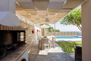 An outdoor patio with a grill, table, chairs, and a pool.