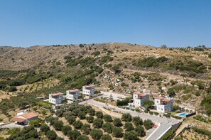 A hillside residential area with modern houses, a swimming pool, and a clear sky.