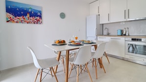 A modern kitchen with white cabinets, a dining table with four chairs, and a colorful painting on the wall. - Holiday Home Rosemary (Slivno)