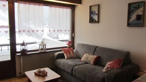 Una sala de estar acogedora con un sofá gris, una mesita y una ventana con cortinas.