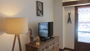 Una sala de estar con un televisor sobre un mueble de madera, una lámpara, un cuadro enmarcado y una ventana con vistas a un paisaje nevado.