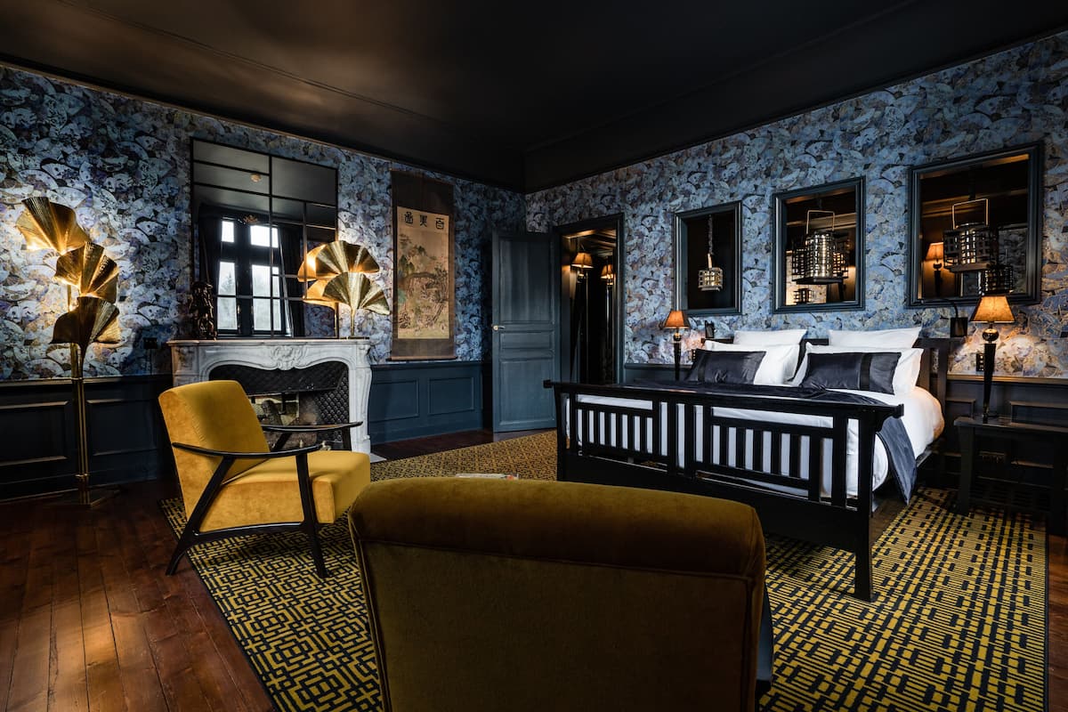 A room with a bed, a chair, a fireplace, and a patterned wall.