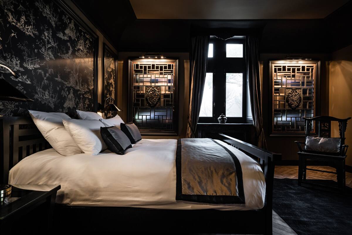 A bedroom with a large bed, a nightstand, a chair, and decorative windows with intricate designs.