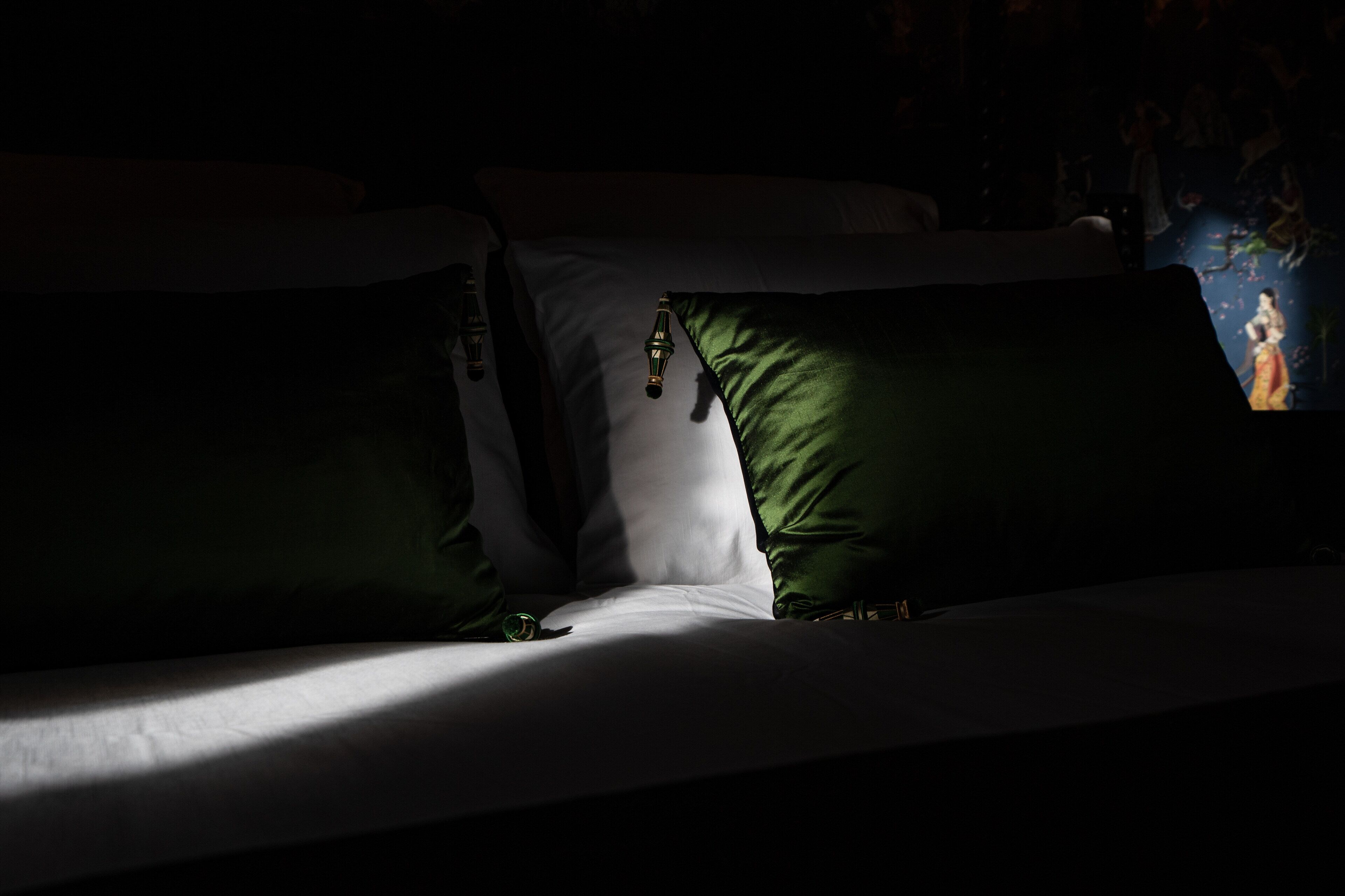 Um quarto com pouca luz, com uma cama adornada por almofadas verdes e brancas.