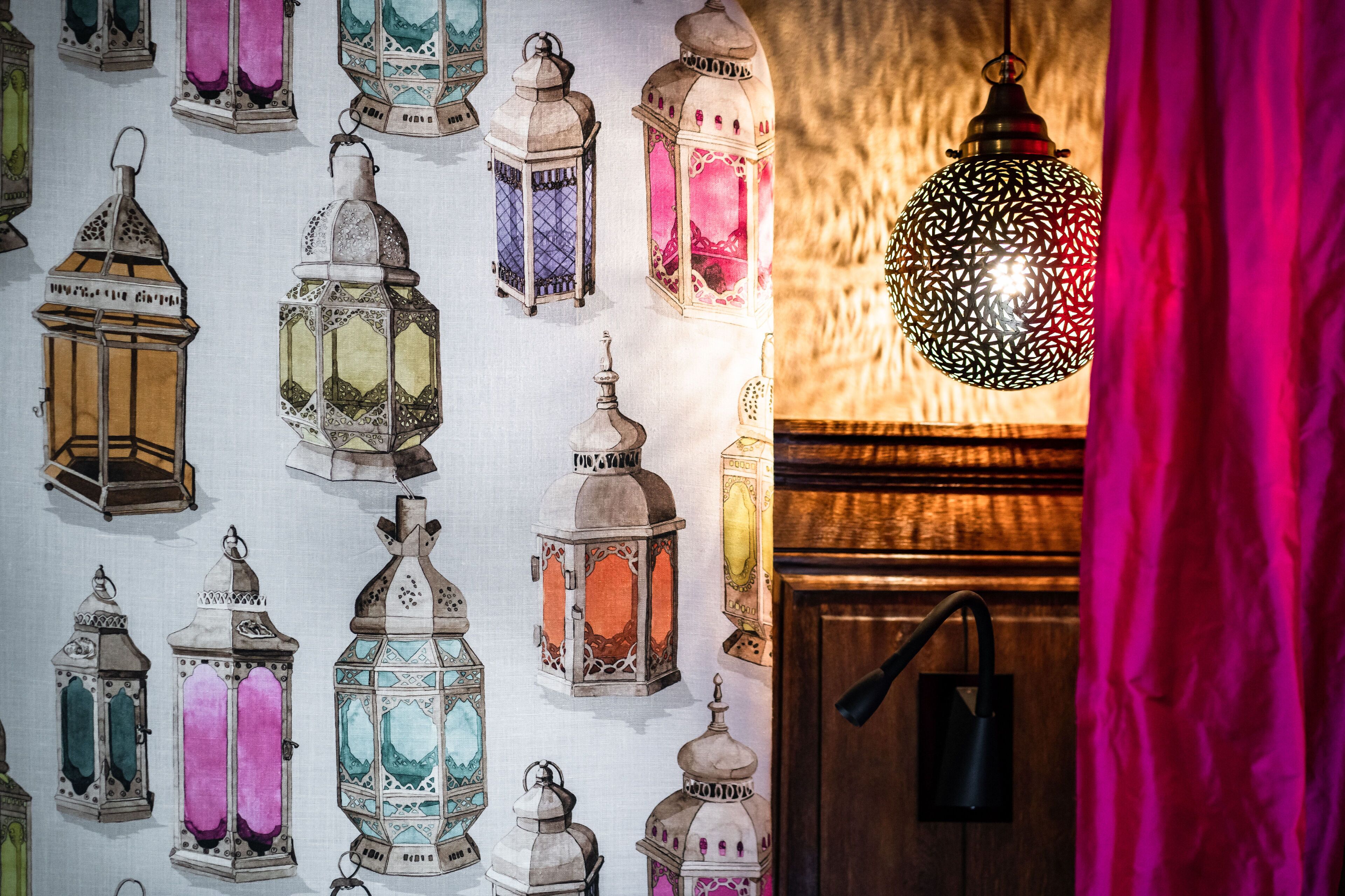A wall with variously designed lanterns and a single hanging lantern.