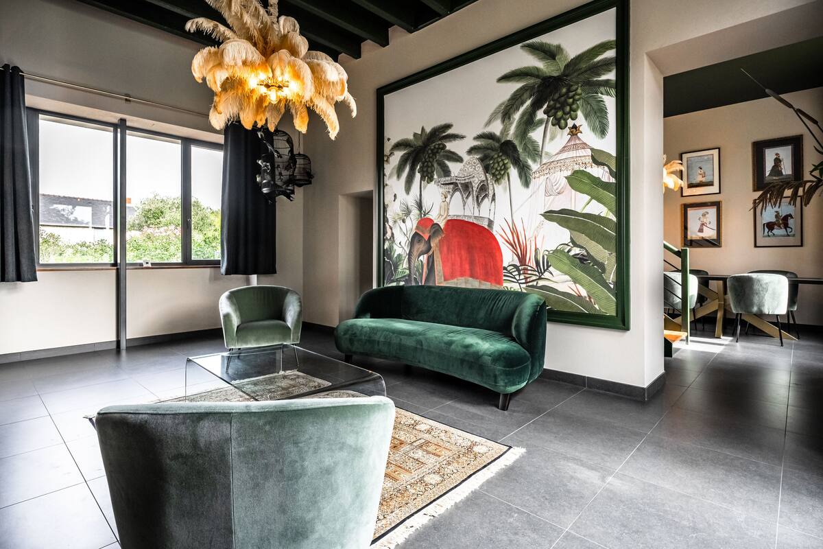 A modern living room with a green sofa, a glass coffee table, and a large tropical mural on the wall.