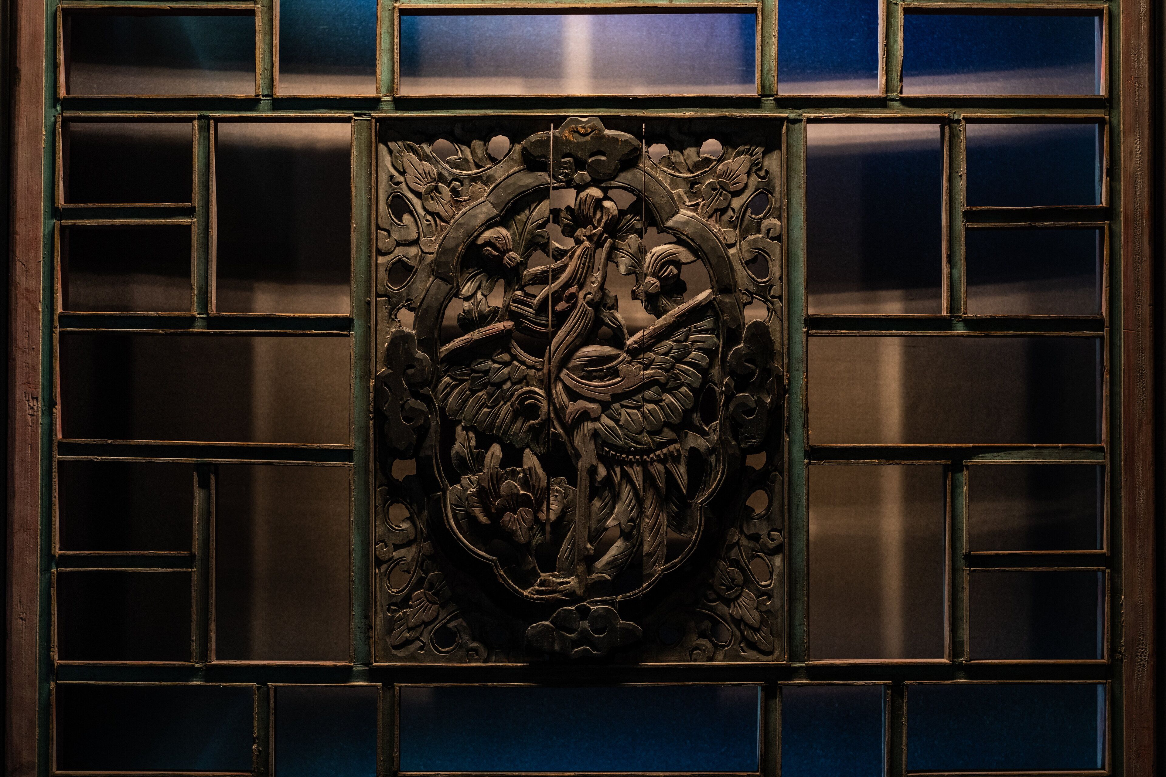 Un panel de madera tallado con detalle, con una figura central, rodeada de diseños geométricos y motivos florales.