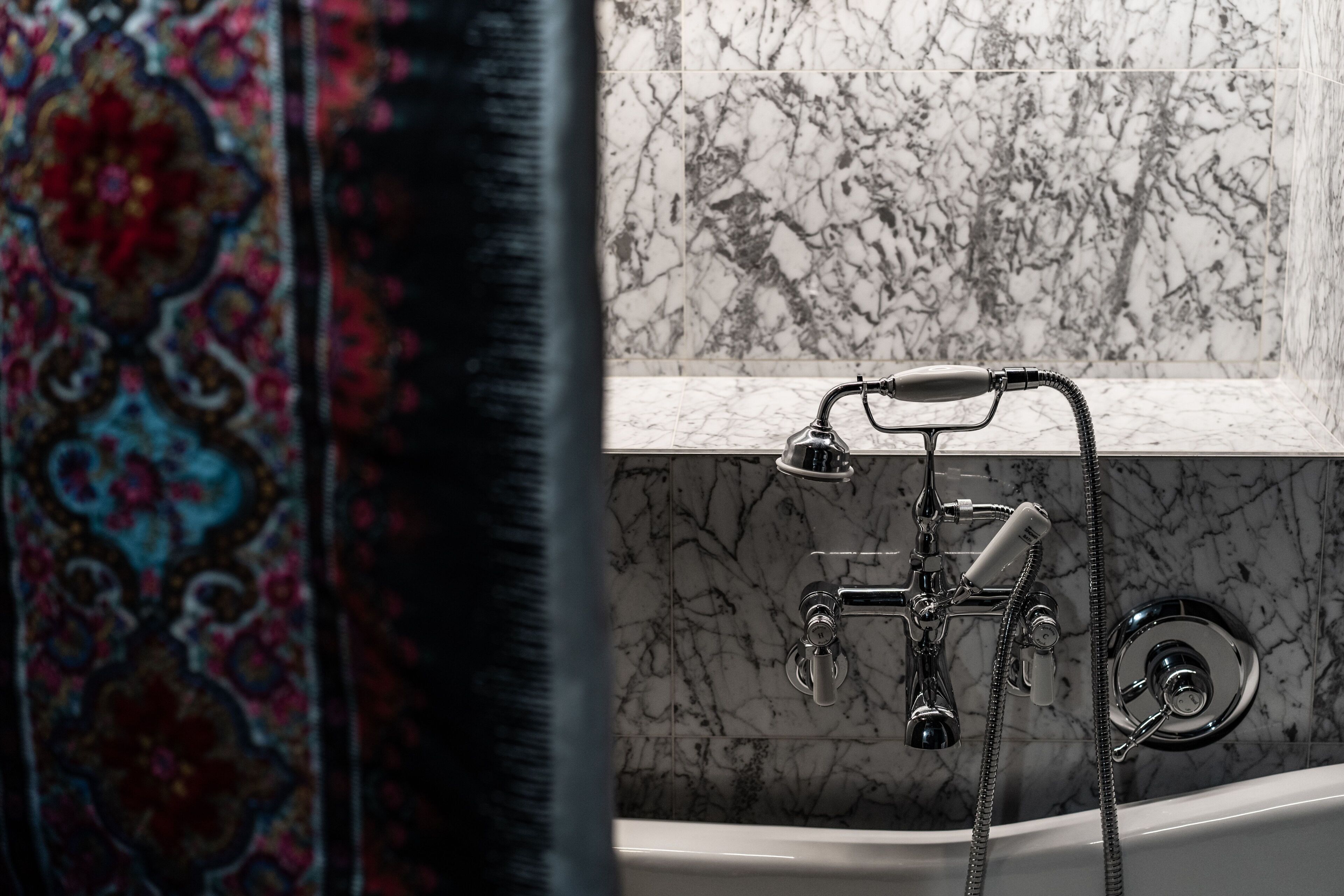 A bathroom with a bathtub, a shower, and a marble wall.