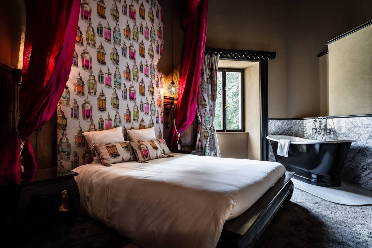 A bedroom with a large bed, a black bathtub, and a patterned wall.