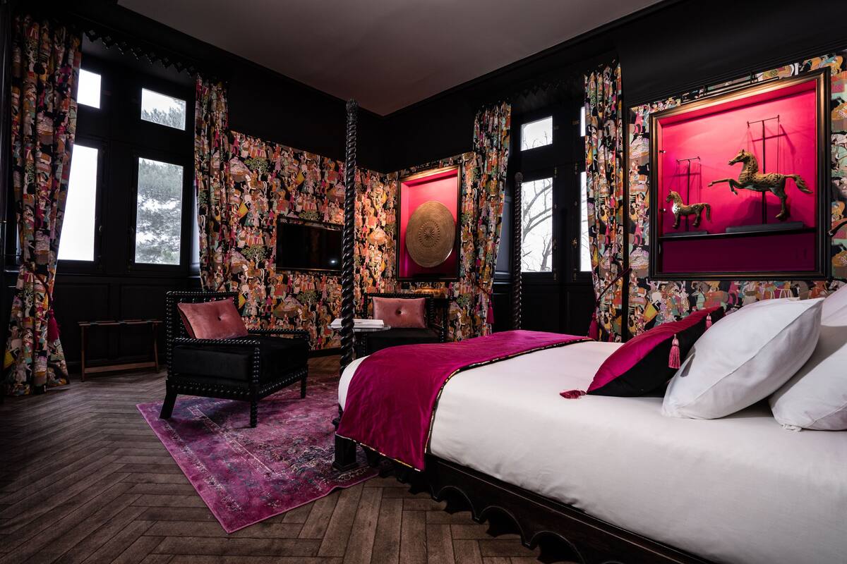 A bedroom with a large bed, a chair, a desk, and a wall with a colorful mural.