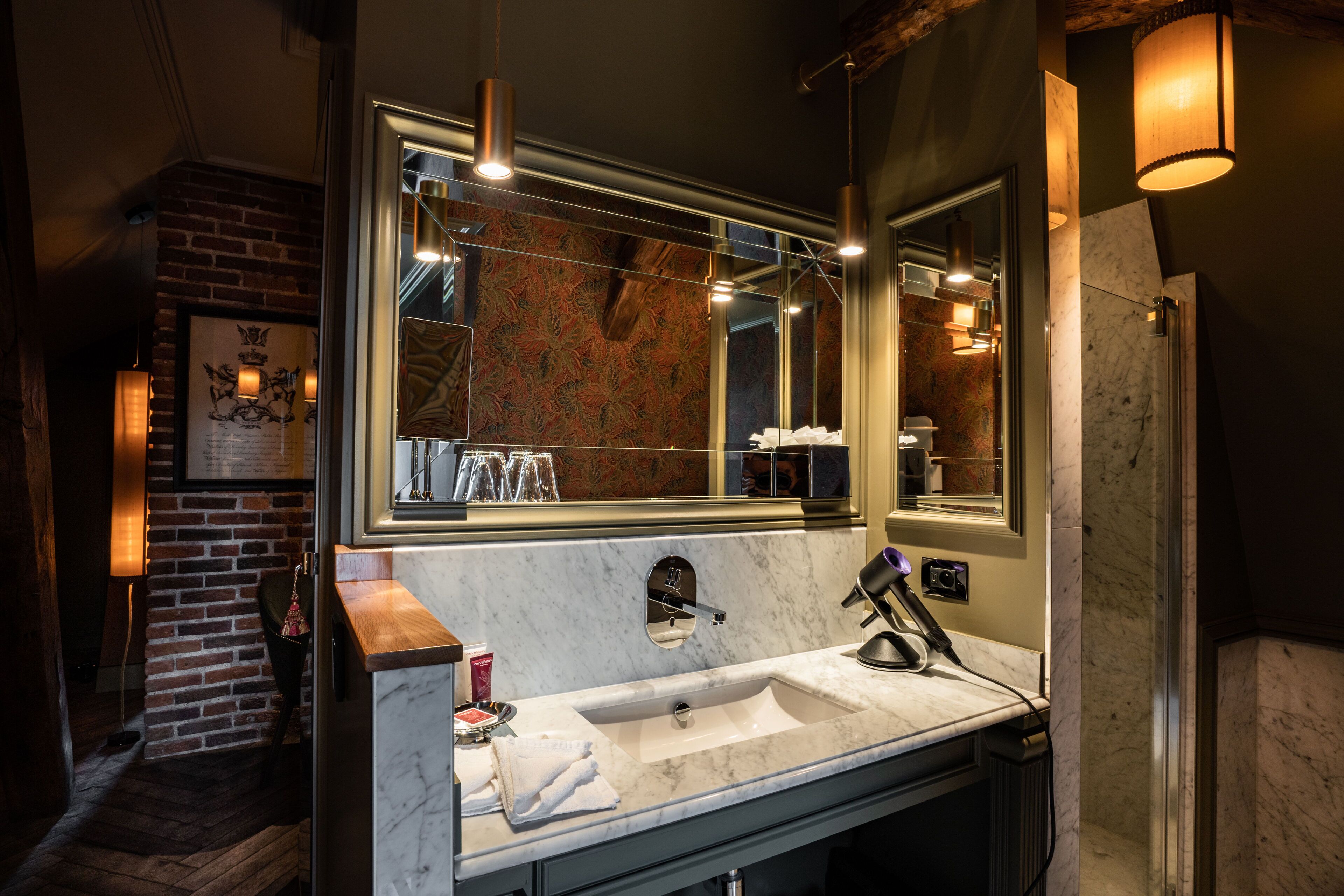 A modern bathroom with a large mirror, a marble sink, and a brick wall.
