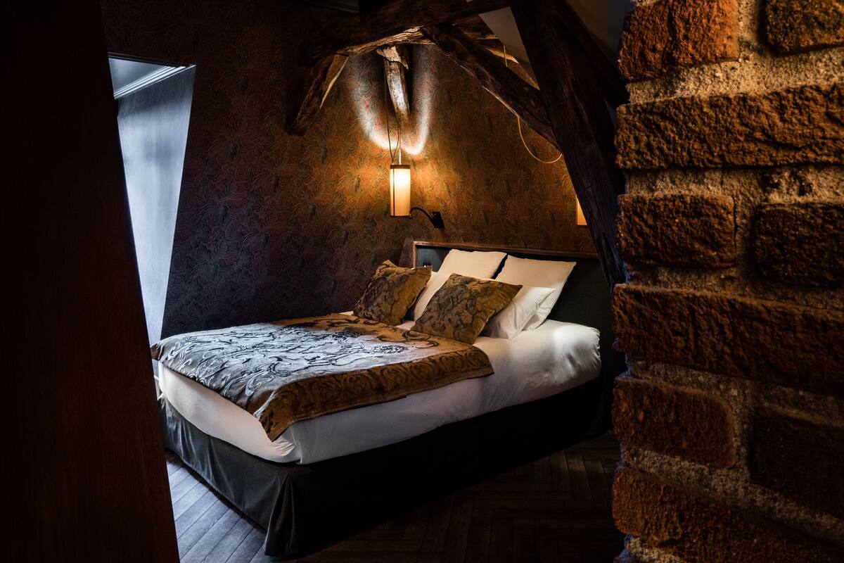 A bedroom with a bed, a wall-mounted light, and a brick wall.