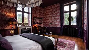 A room with a large bed, a fireplace, a desk, and a view of the outside.