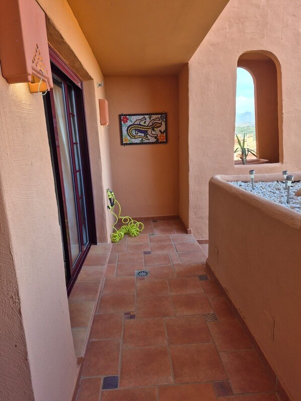 Un estrecho pasillo con suelo de baldosas, un mosaico decorativo en la pared y una ventana con vistas al desierto.