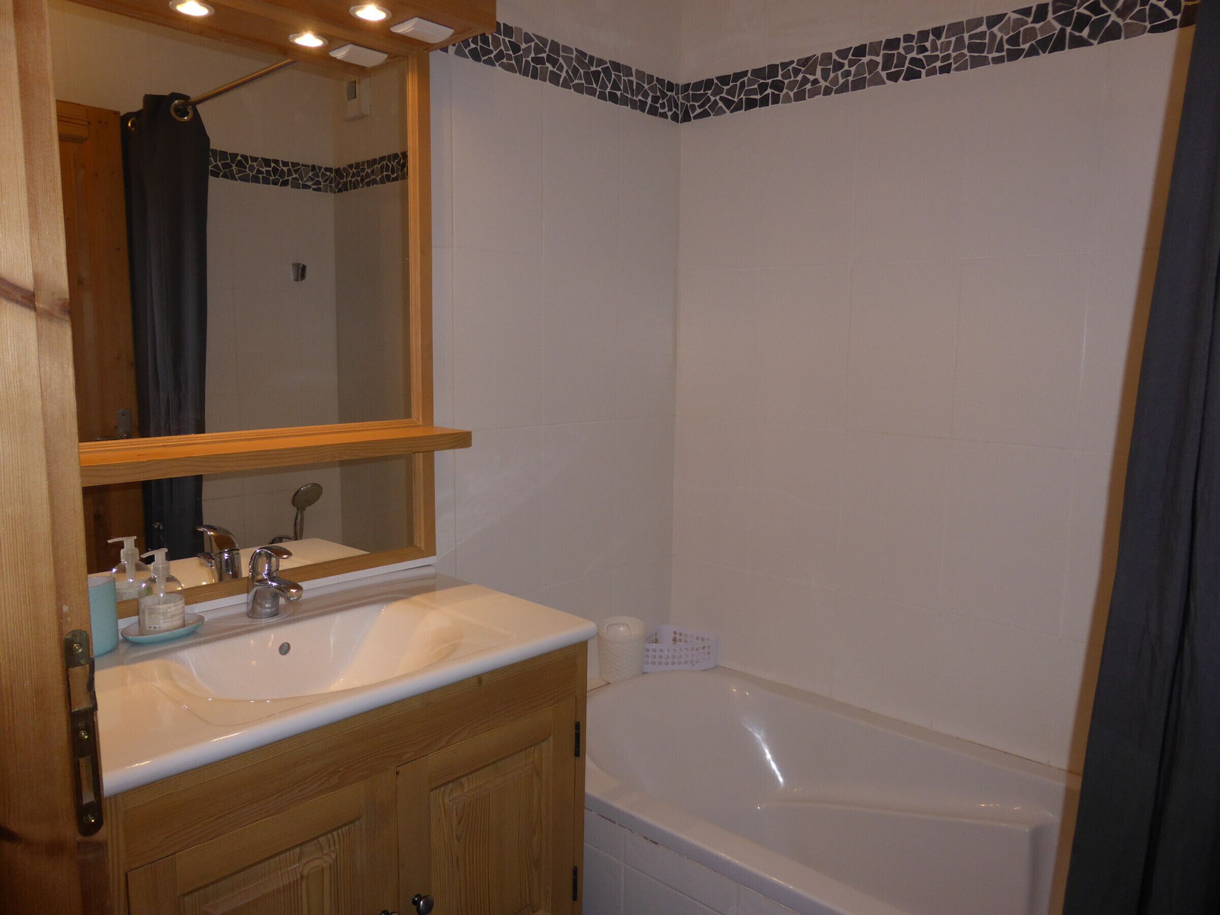 A bathroom with a wooden vanity, a sink, a mirror, a bathtub, and a shower curtain.