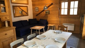 Una cabaña acogedora de madera con comedor para cuatro, un sofá y una lámpara.