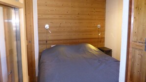 Un dormitorio con cabecera de madera, cama con manta gris y dos lámparas de noche.
