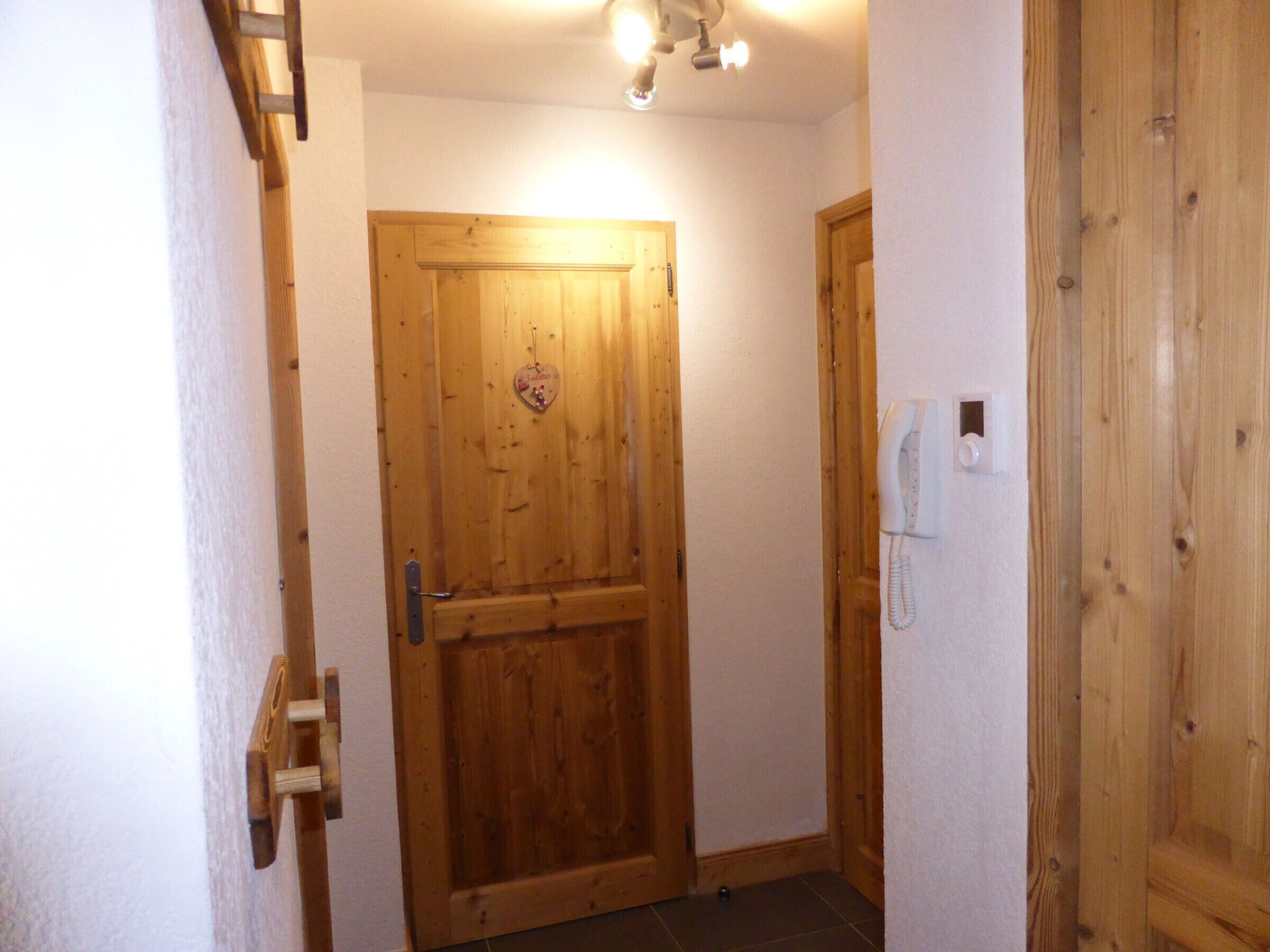 A wooden door with a heart-shaped decoration, a wall-mounted phone, and a light fixture above.