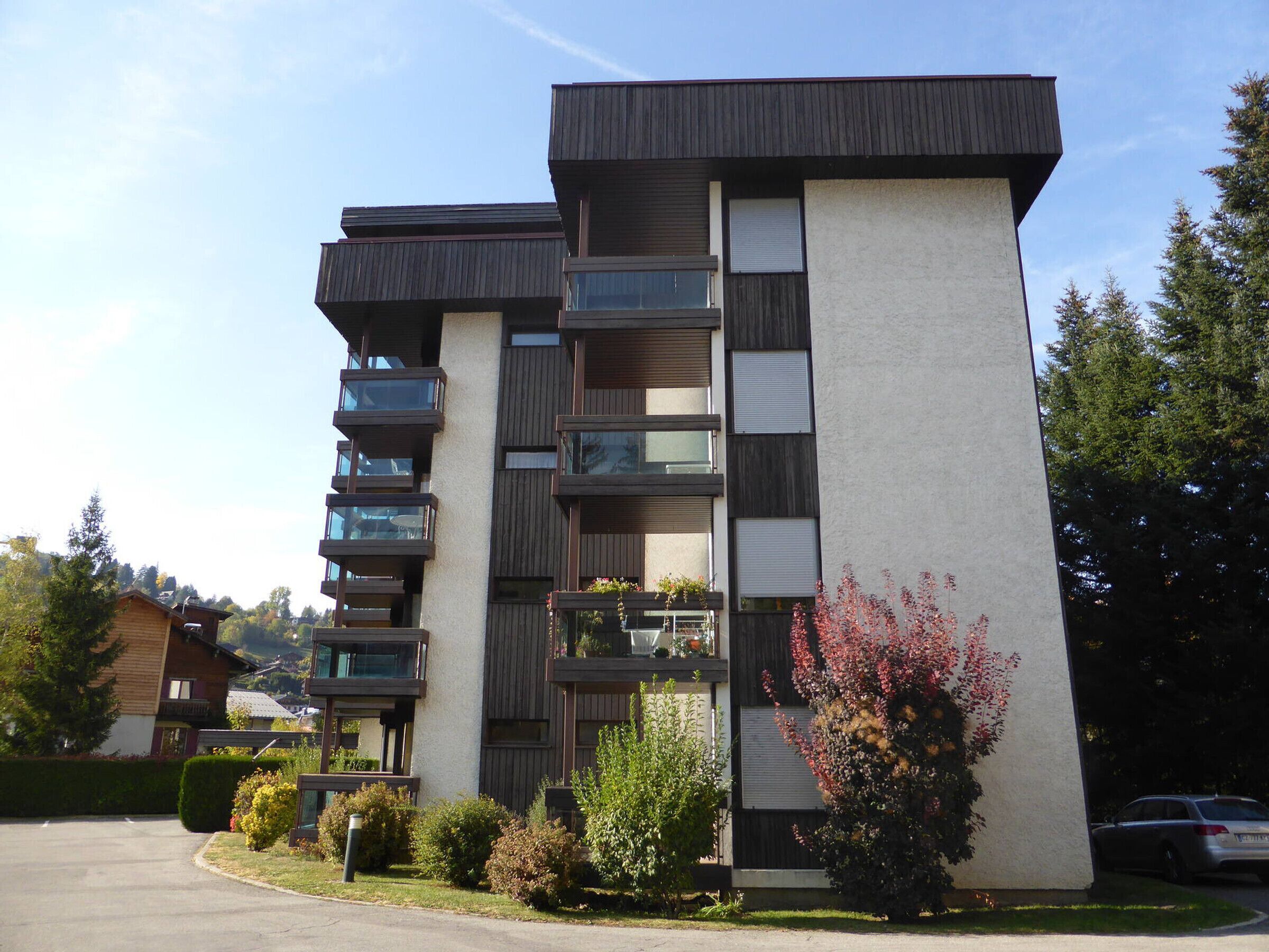 Un immeuble d’appartements moderne, à plusieurs étages, doté de balcons, d’une cour intérieure et entouré de verdure.