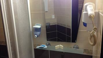 A bathroom with a mirror, a hand dryer, a paper towel dispenser, and a glass shelf with toiletries.