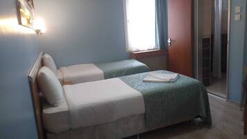 A room with two beds, a window with curtains, an air conditioning unit, and a door leading to a bathroom.