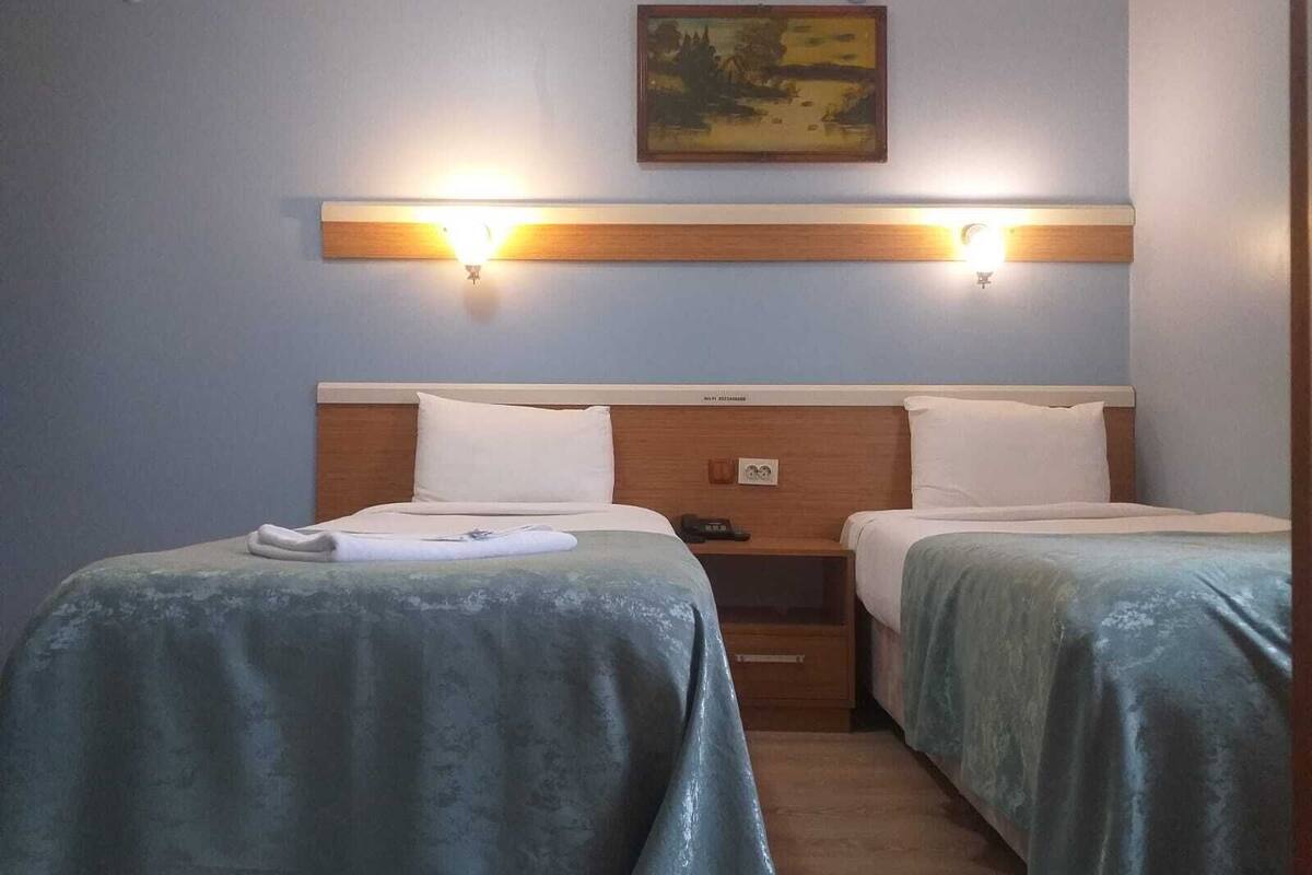A hotel room with two single beds, wooden headboards, and a painting above the beds.