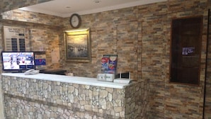 A reception area with a stone counter, a clock, a television displaying room rates, and a framed picture on the wall. - Hotel Oz Villa (Istanbul)