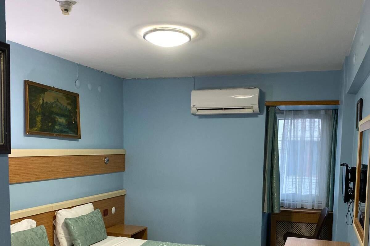 A hotel room with a bed, a desk, an air conditioning unit, and a painting on the wall.