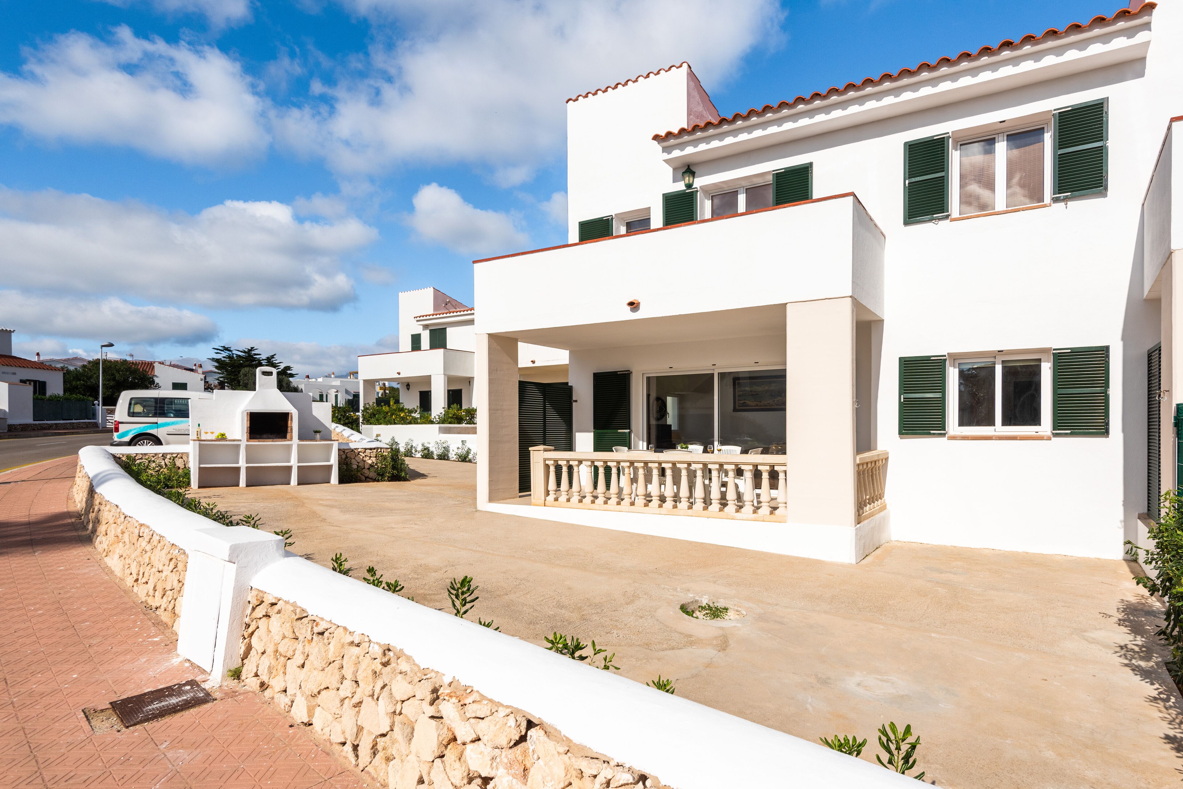 Una casa moderna de dos pisos con un balcón, un muro de contención de piedra y un camino de entrada pavimentado.