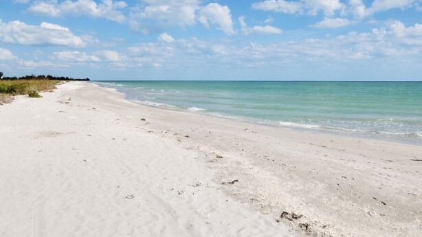 Ein sandiger Strand mit klarem, blauem Wasser und einem teilweise bewölkten Himmel.