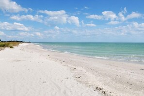 Ein sandiger Strand mit klarem, blauem Wasser und einem teilweise bewölkten Himmel.