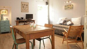 A cozy room with a wooden table, chairs, a bed with pillows, a TV, and artwork on the walls.